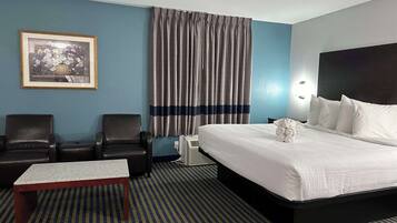 Una habitación de hotel con una cama, dos sillones, una mesita, aire acondicionado de pared y un cuadro enmarcado.