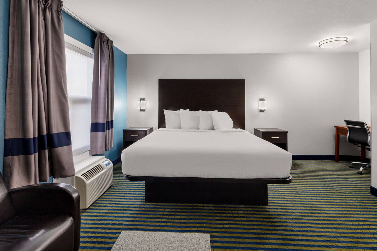 Ein Hotelzimmer mit einem großen Bett, einem Schreibtisch, einem Sessel, einem Heizkörper und Vorhängen.