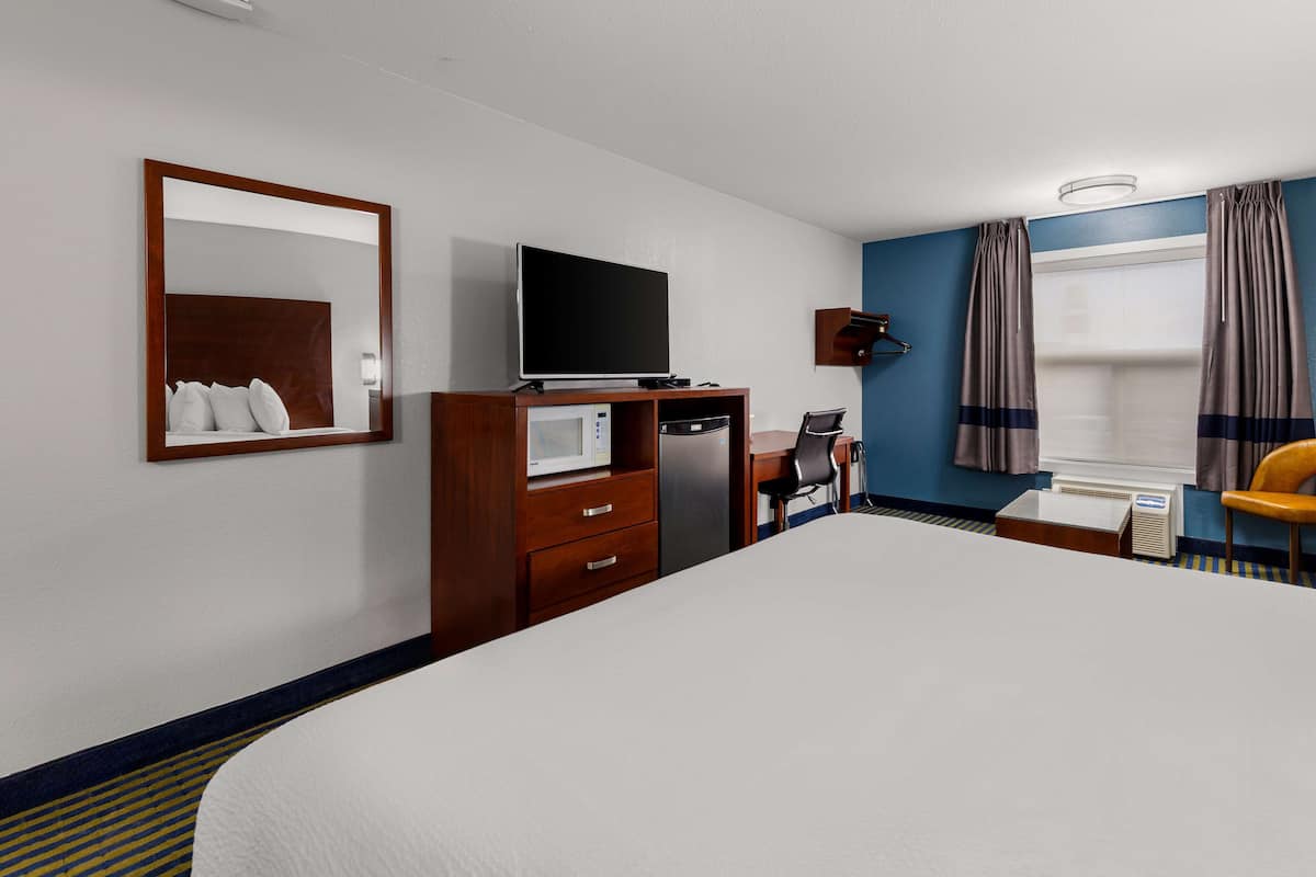 Ein Hotelzimmer mit einem großen Bett, einem Schreibtisch, einem Flachbildfernseher, einer Mikrowelle und einem Sessel.