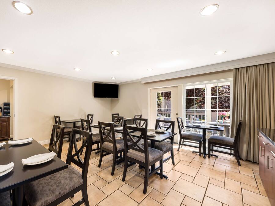 A dining area with multiple tables and chairs, a flat-screen TV mounted on the wall, and a view of the outside through large windows.