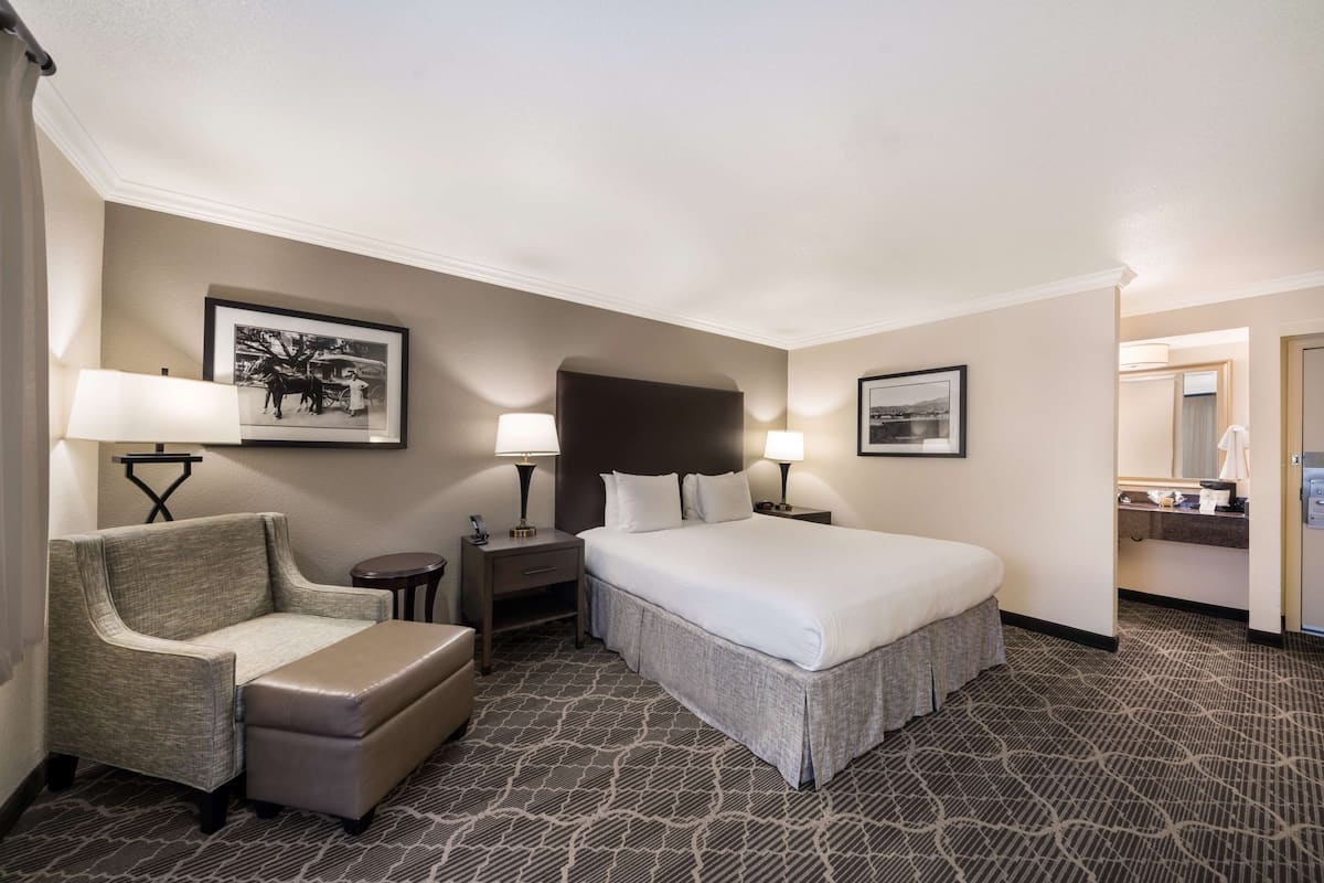 A hotel room with a large bed, a chair, a small table, and two lamps.