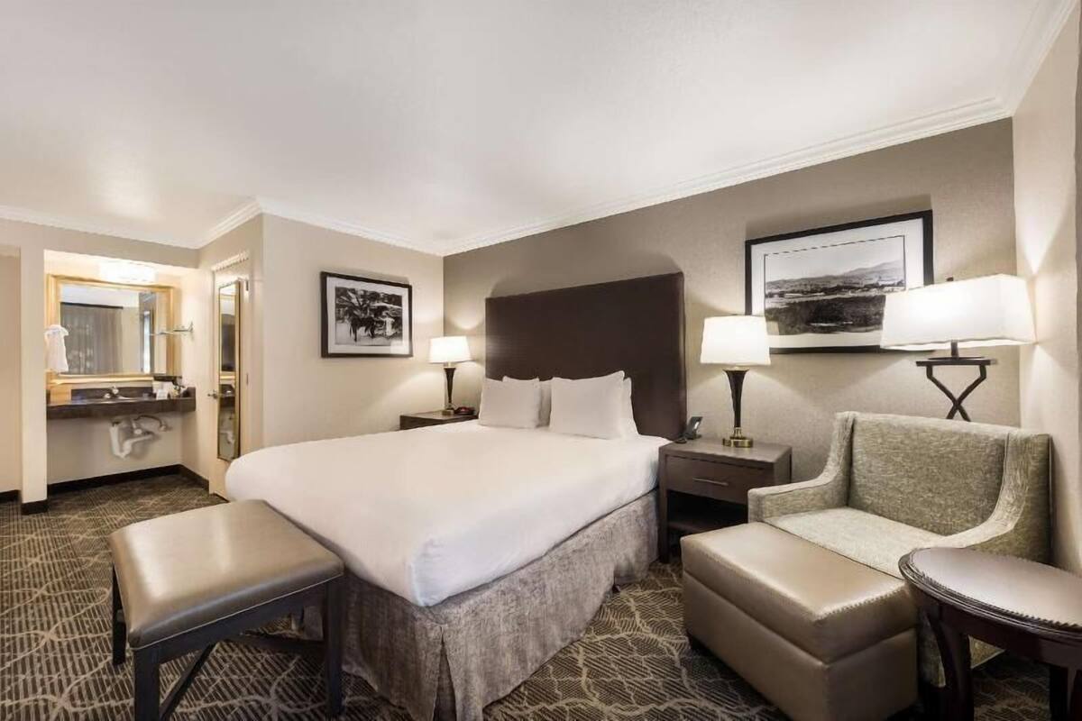 A hotel room with a large bed, two bedside tables, a chair, a desk, a mirror, and artwork on the walls.