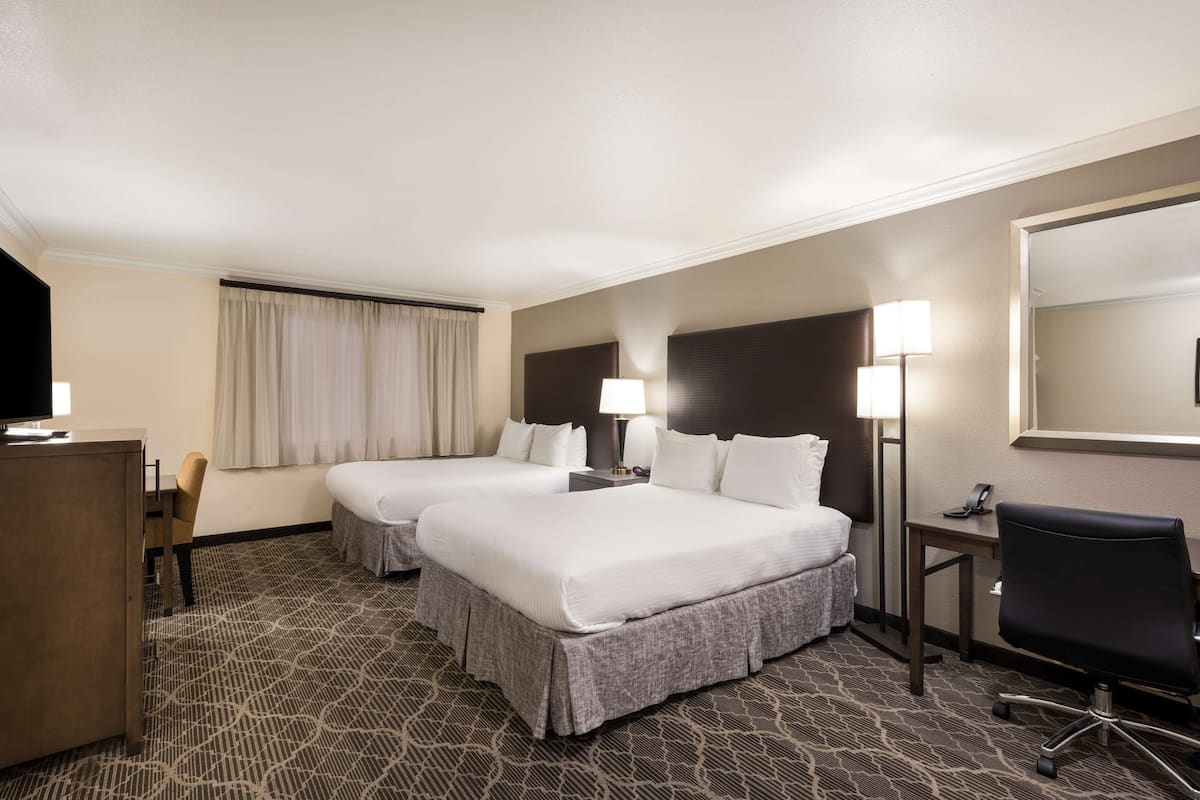 A hotel room with two beds, a desk, a chair, and a large mirror.