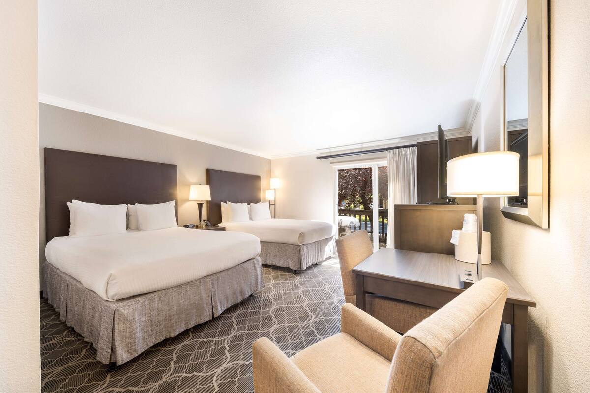 A hotel room with two beds, a desk, a chair, and a large window.