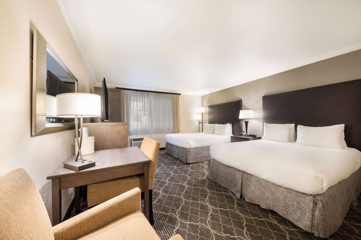 A hotel room with a large bed, a desk, a chair, and a small table.