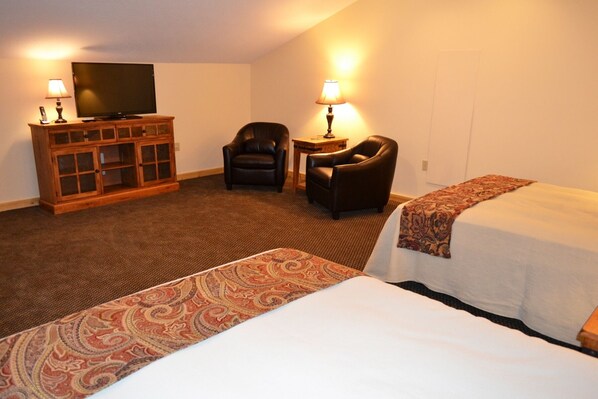 A hotel room with two beds, a TV, a wooden cabinet, two chairs, and two lamps.