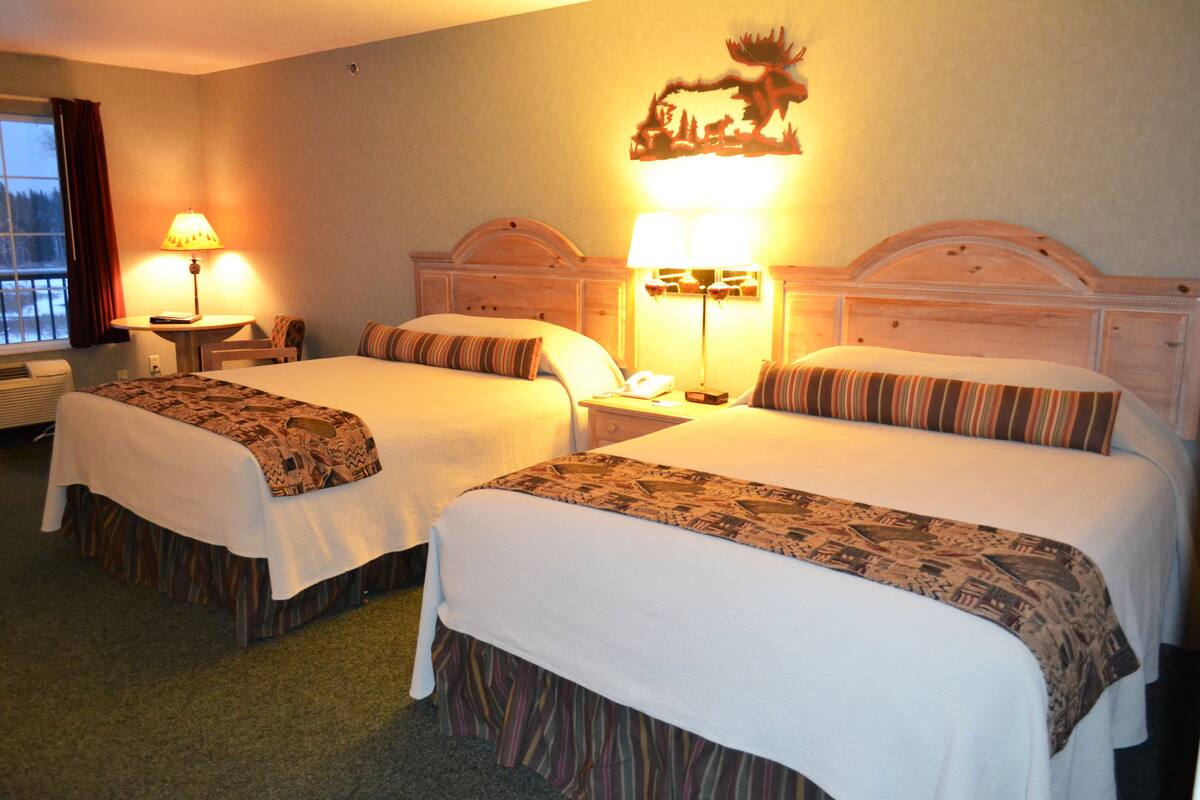 Ein Hotelzimmer mit zwei Betten, jedes mit einer gemusterten Tagesdecke, einem Nachttisch mit Lampe und einem dekorativen Wandbild über den Betten.