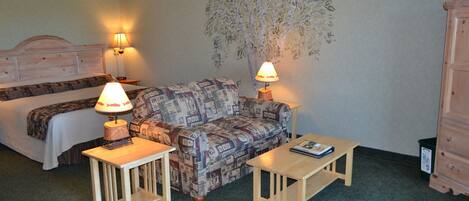A room with a bed, a patterned sofa, two small tables with lamps, and a wall mural.