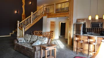Un salon chaleureux avec un canapé, une table basse en bois et un escalier menant à l’étage supérieur.