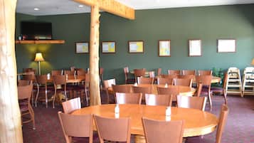 A dining area with multiple round tables and chairs, a television mounted on the wall, and framed certificates on the wall.