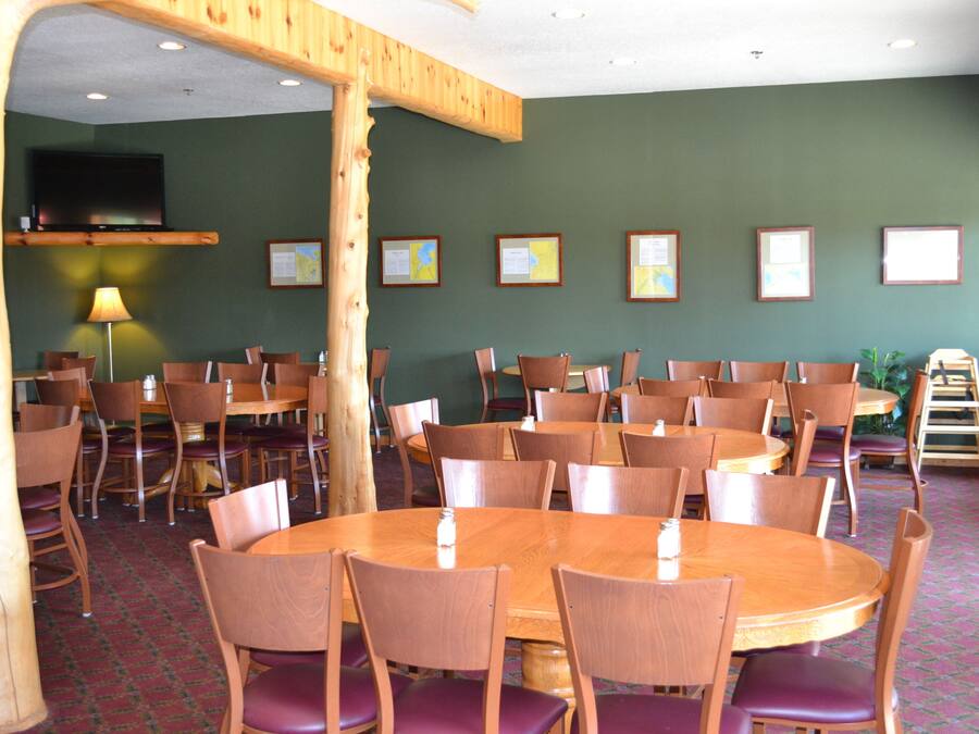 A dining area with multiple round tables and chairs, a television mounted on the wall, and framed certificates on the wall.