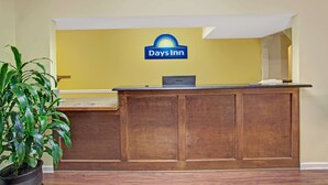 A reception desk with a Days Inn logo, a potted plant, and a wooden counter. - Days Inn by Wyndham Marietta White Water (Marietta)