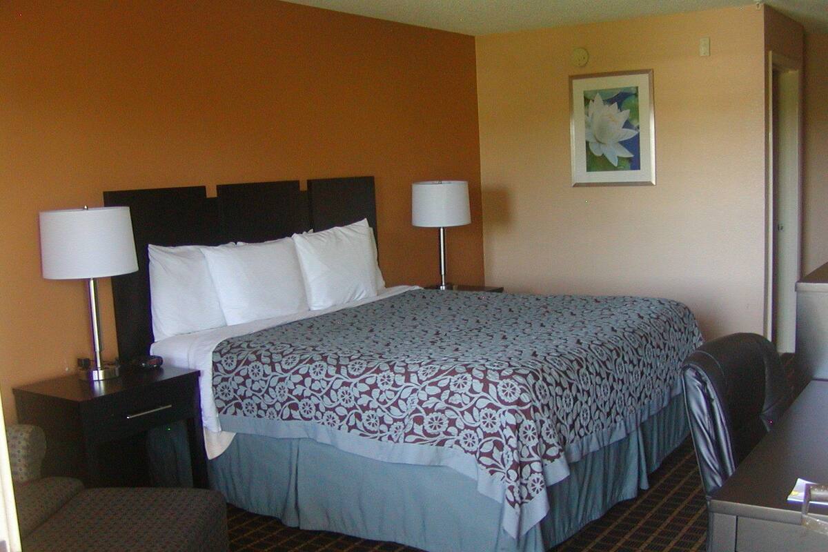 A hotel room with a large bed, two bedside lamps, a desk with a chair, and a framed picture on the wall.