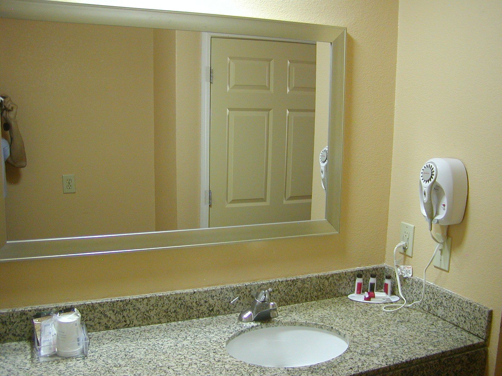 A bathroom with a large mirror, a sink, a hairdryer, and toiletries.