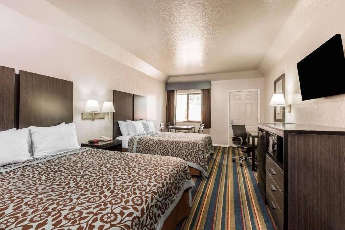 A hotel room with two beds, a desk, a chair, a TV, and a window.