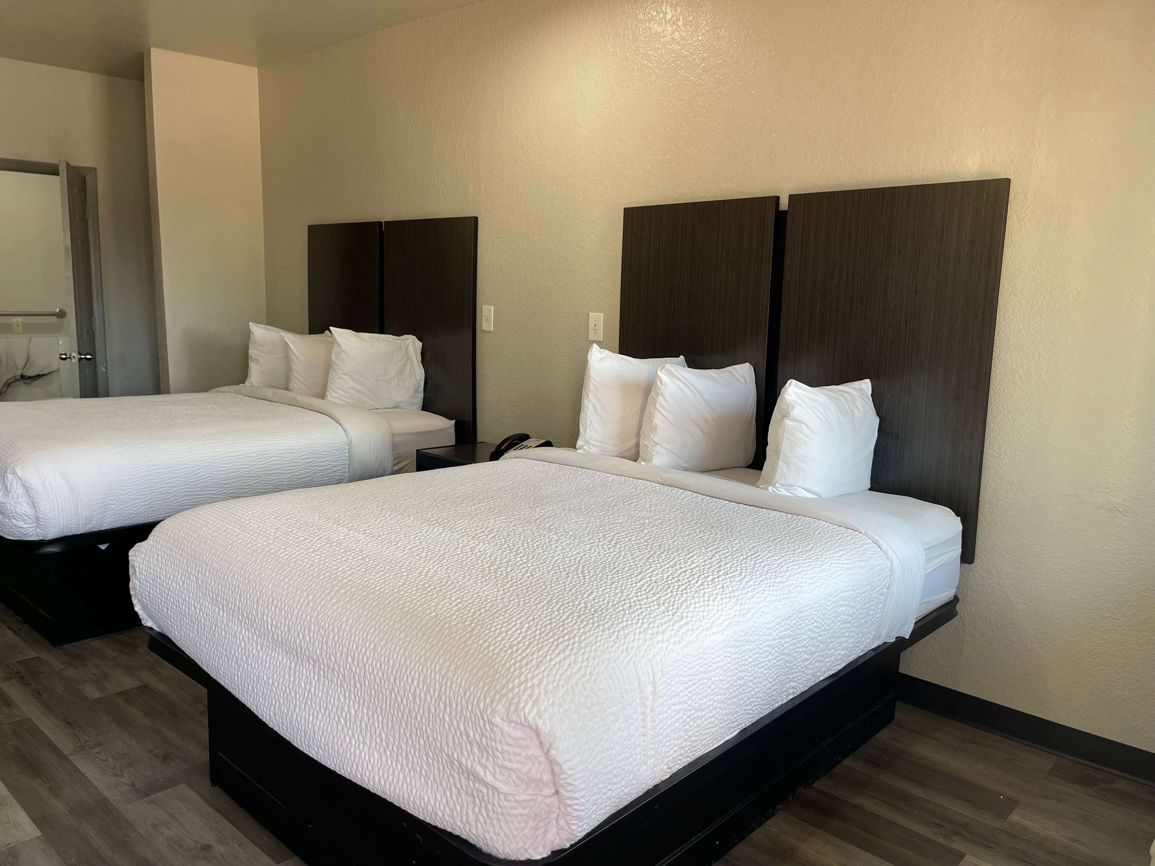 Duas camas de solteiro com roupa de cama branca e cabeceiras escuras em um quarto de hotel.
