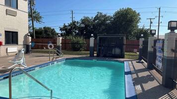 Relax by the pool surrounded by lush greenery and a brick building.