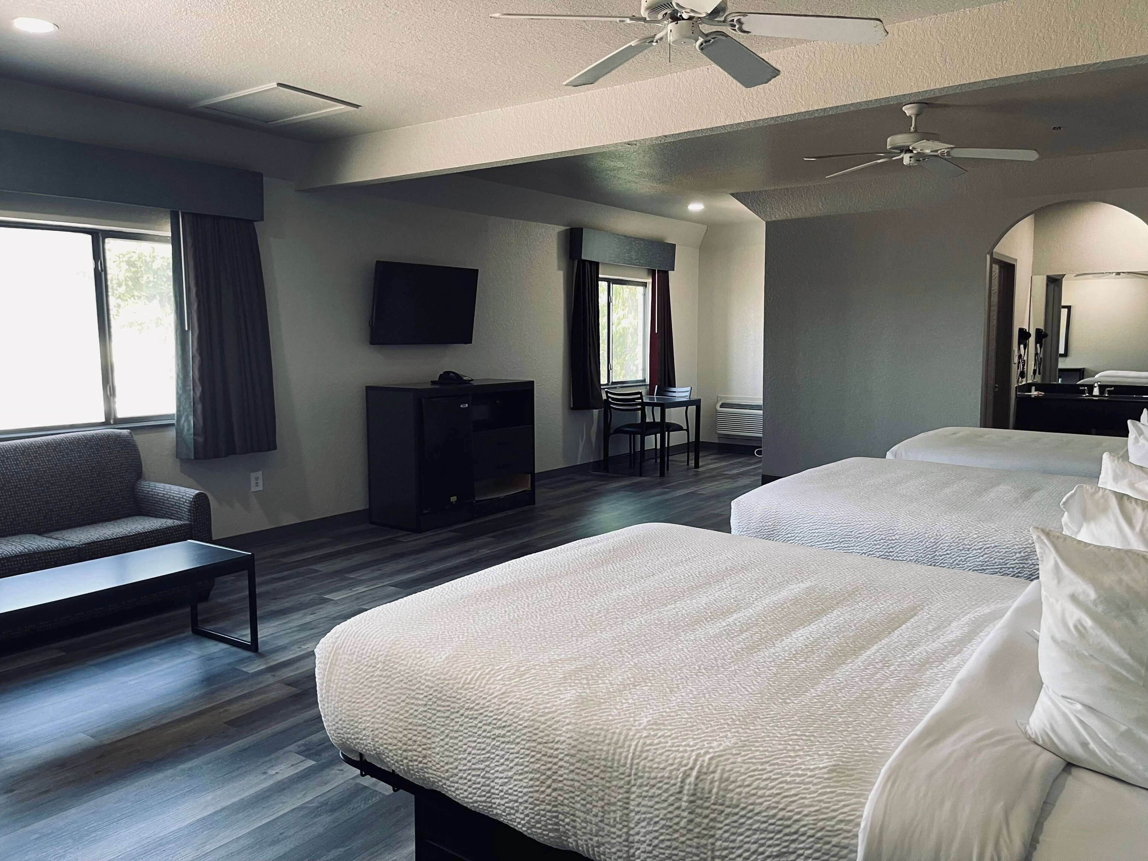 A hotel room with two beds, a sofa, a TV, a ceiling fan, and a window with curtains.