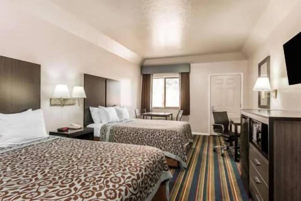 A hotel room with two beds, a desk, a chair, a dresser, and a television.