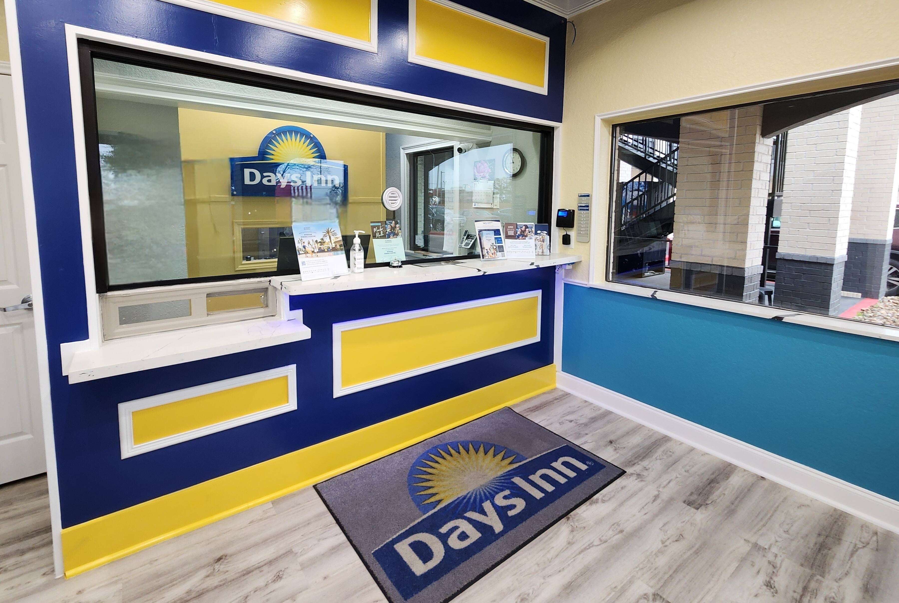A reception area with a blue and yellow color scheme, a reception desk, a glass window, and a doormat with the Days Inn logo.