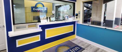 A reception area with a blue and yellow color scheme, a reception desk, a glass window, and a doormat with the Days Inn logo.