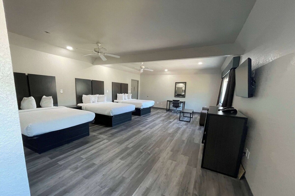 A hotel room with three beds, a desk, a chair, a TV, and a ceiling fan.