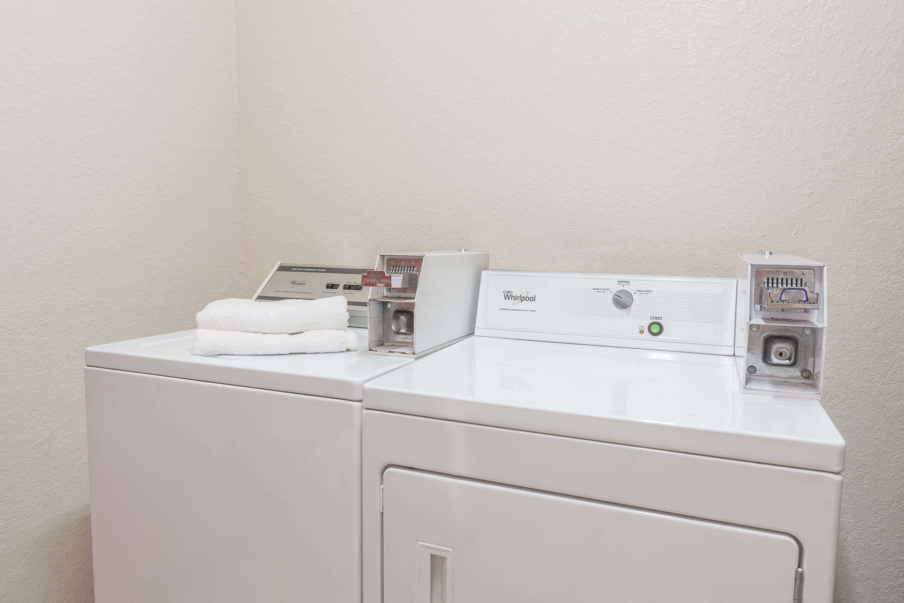 Un appareil combiné lave-linge et sèche-linge Whirlpool à chargement frontal, doté d’un panneau de commande, d’une serviette blanche posée sur le dessus et d’une prise électrique fixée au mur.