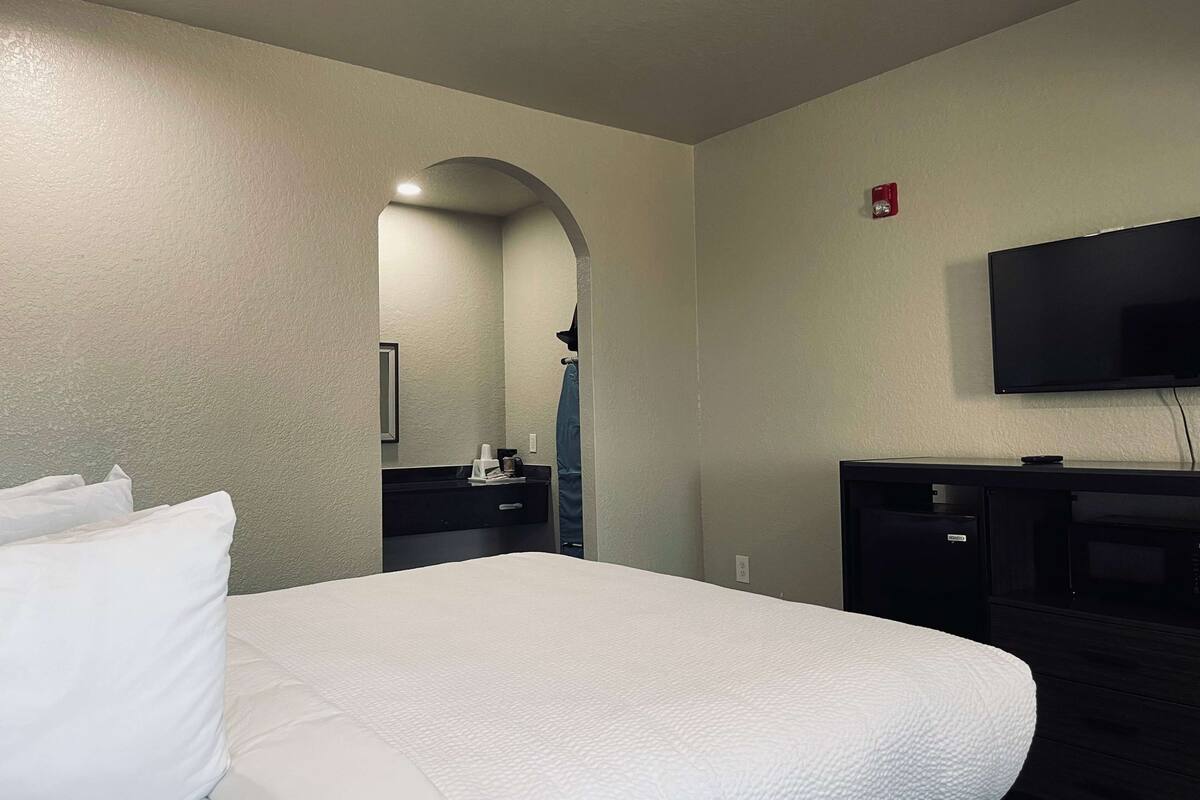 A hotel room with a large bed, a flat-screen TV, a desk, and a mirror.