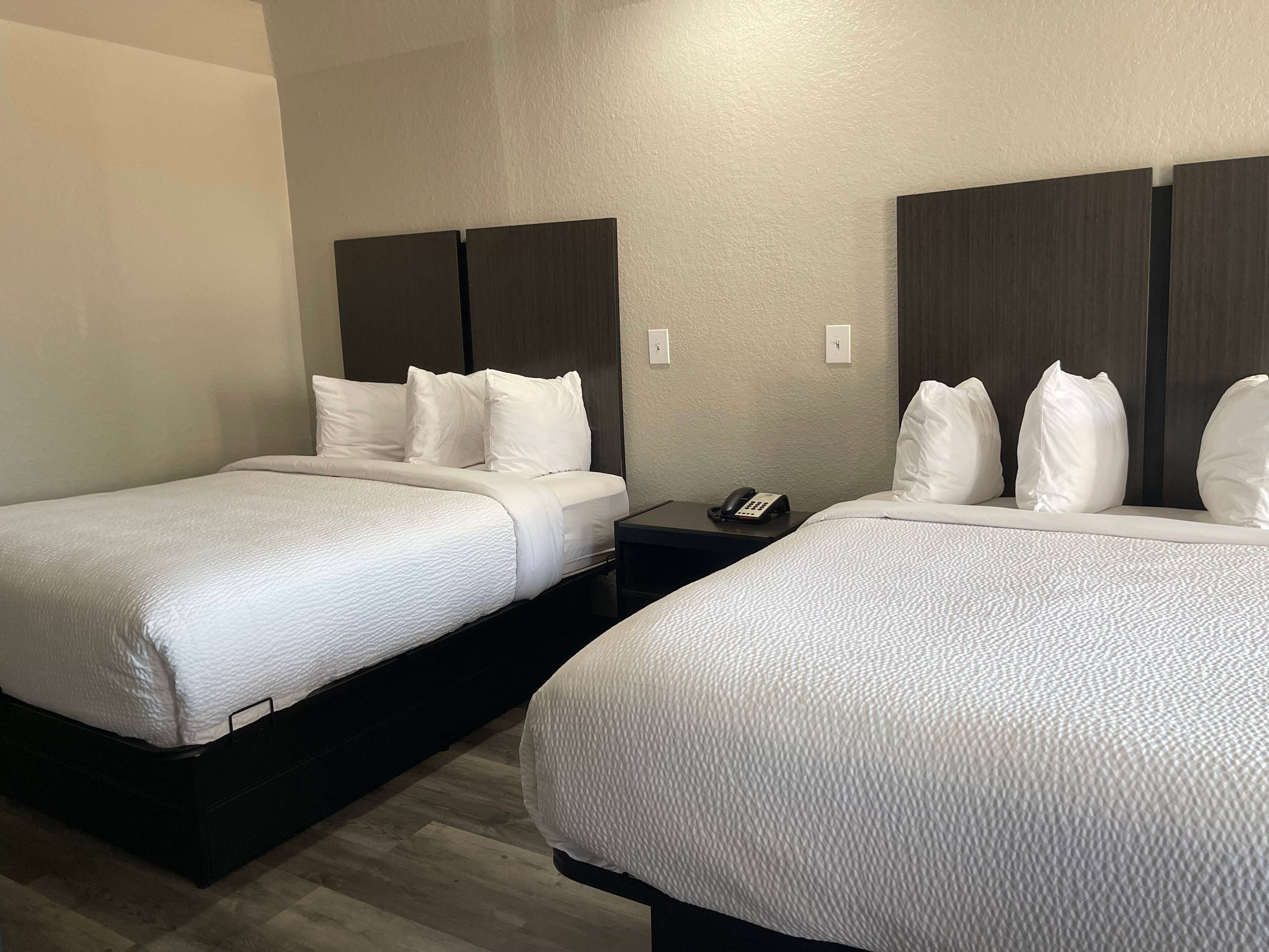 Duas camas de casal com roupa de cama branca, cabeceiras escuras e um telefone de mesa.