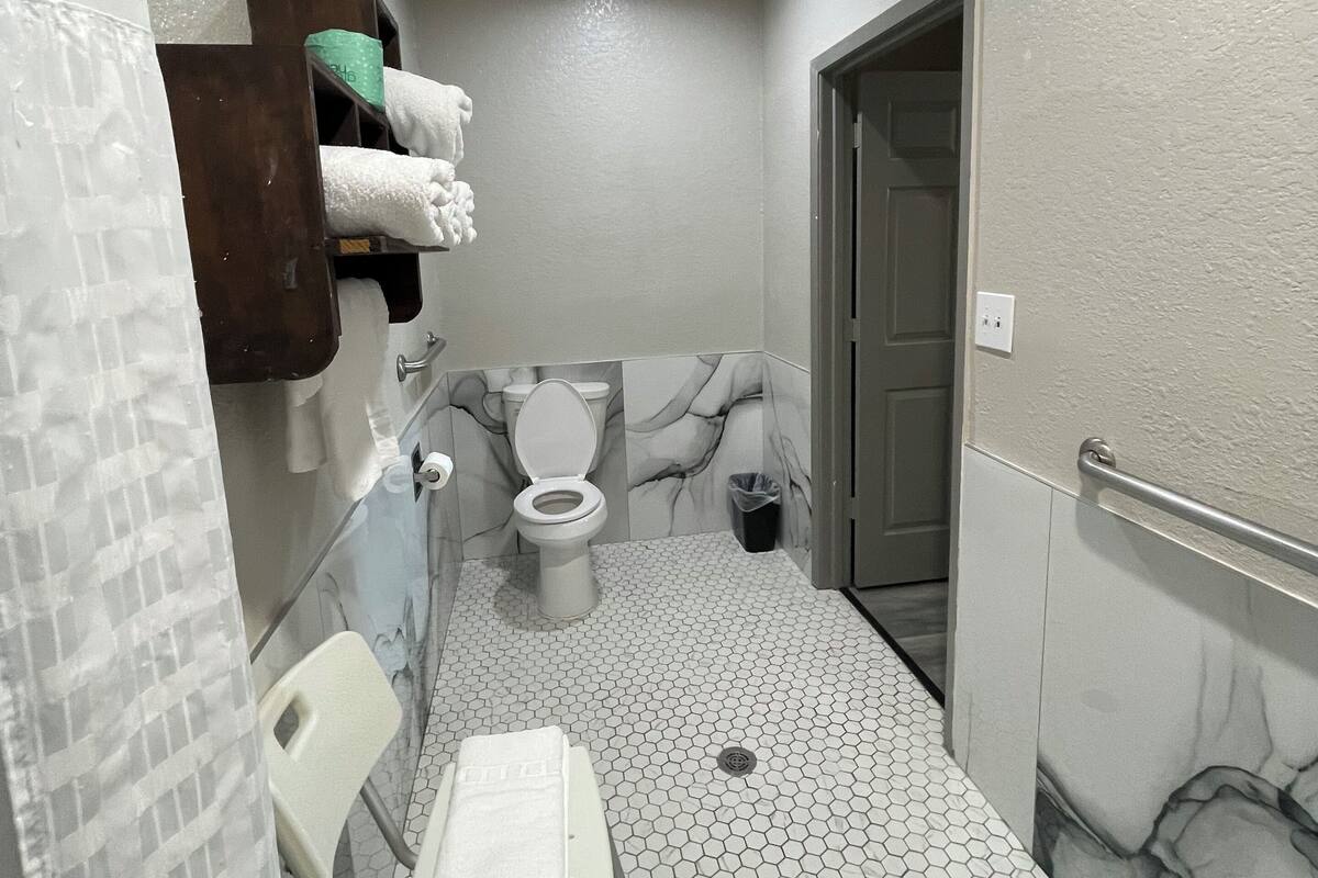 A bathroom with a toilet, a hand dryer, a trash bin, and a shower area.