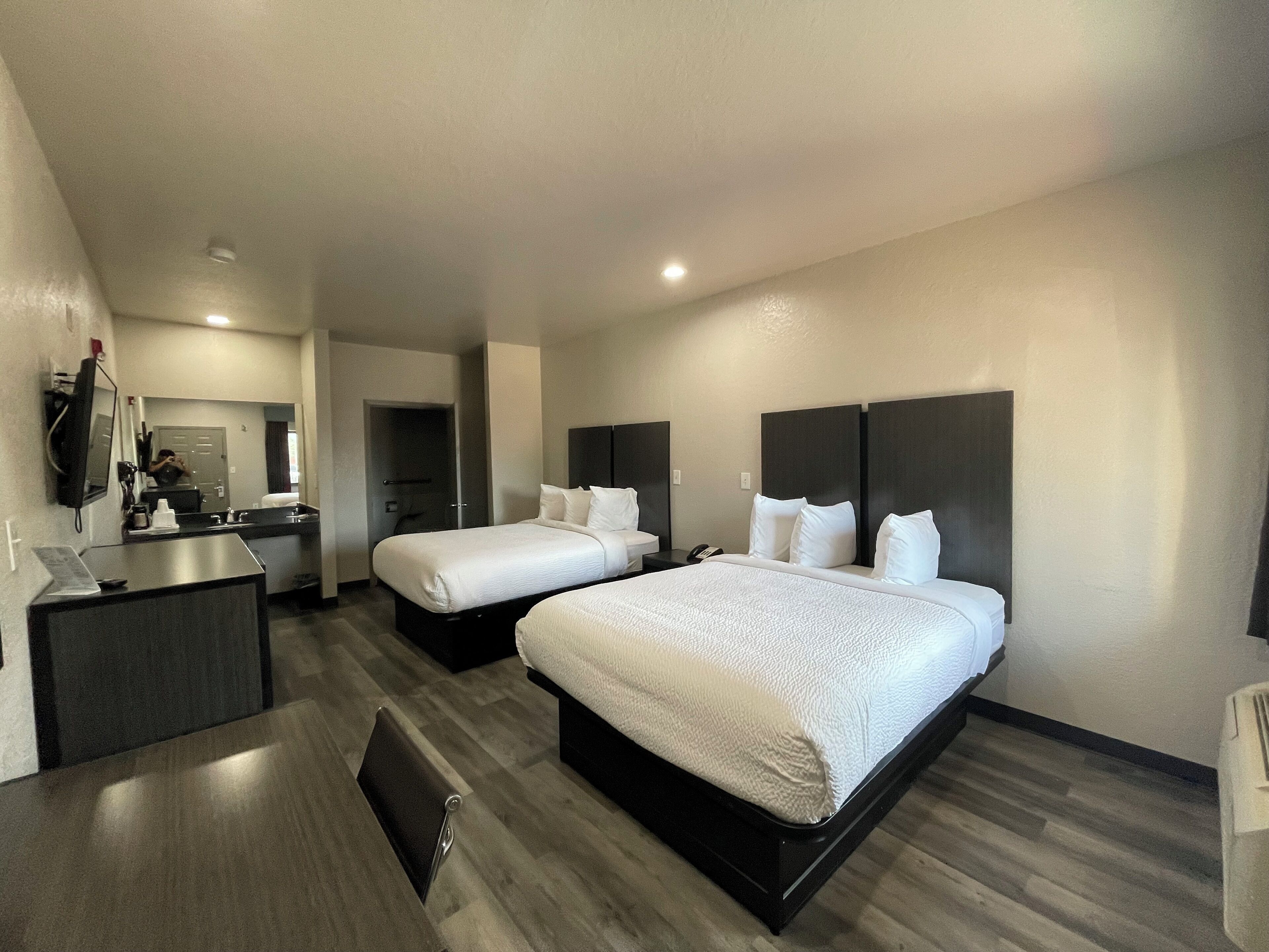 A hotel room with two beds, a desk, and a mirror.