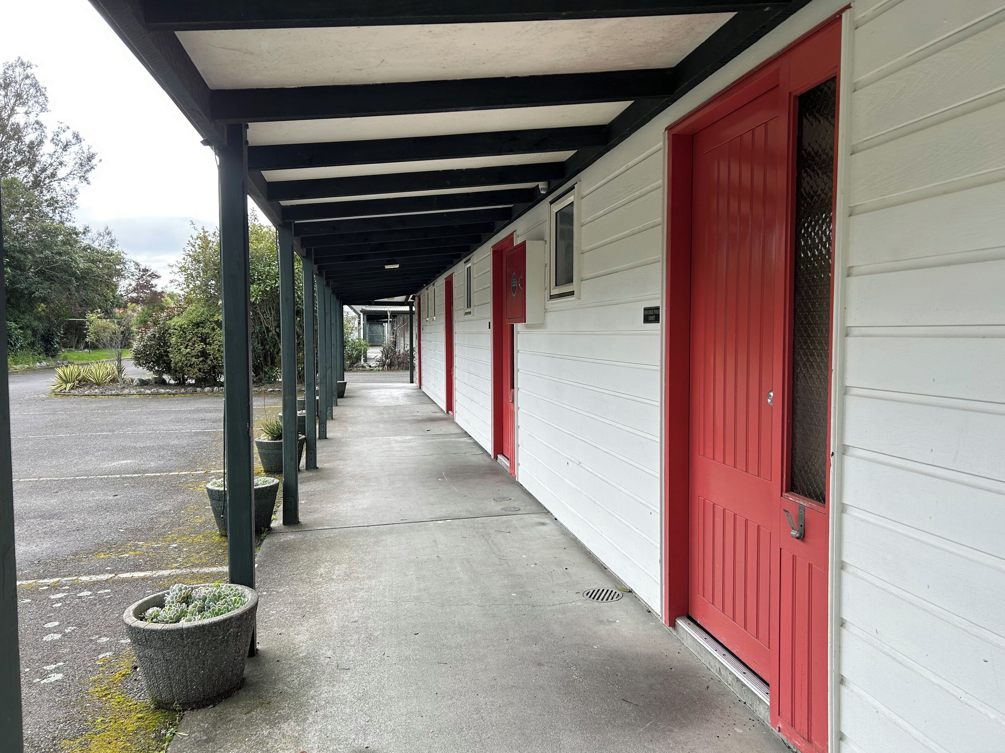 A covered walkway with red doors and a white building.