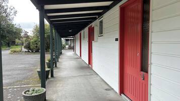 A covered walkway with red doors and a white building.
