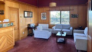 A room with wooden paneling, two sofas, a coffee table, a desk, and a window with a view of greenery.