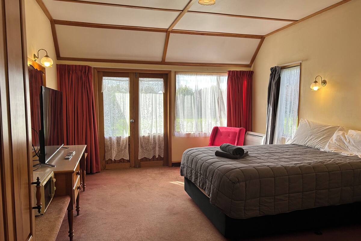 Una habitación de hotel con una cama, un escritorio con computadora, televisión y ventana con cortinas.