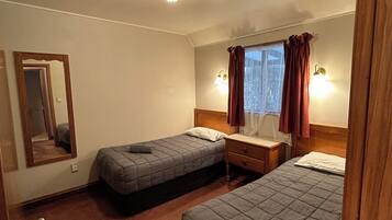 A hotel room with two single beds, a wooden nightstand, a mirror, and a window with curtains.