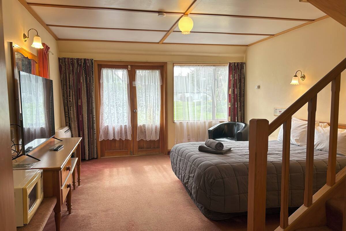 Un dormitorio con cama, escritorio, silla, escalera y ventana con cortinas.