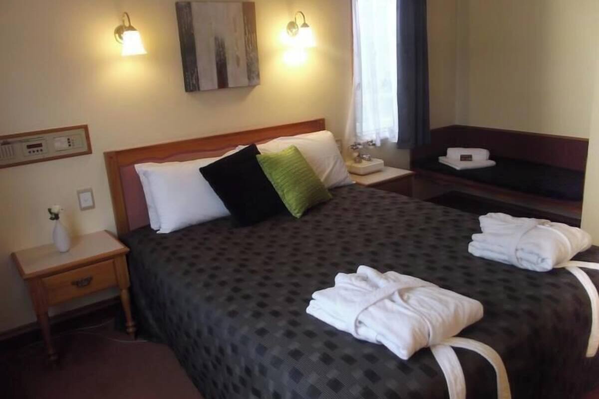 Una habitación de hotel con cama, mesitas de noche, televisor y un cuadro en la pared.