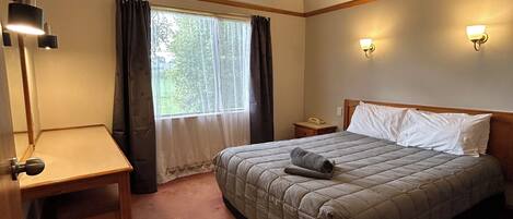 A bedroom with a bed, bedside table, lamp, window with curtains, and wall-mounted lights.