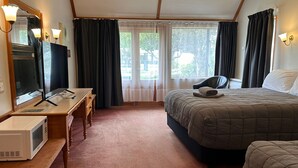 A hotel room with a bed, a desk with a flat-screen TV, a microwave, and a chair.