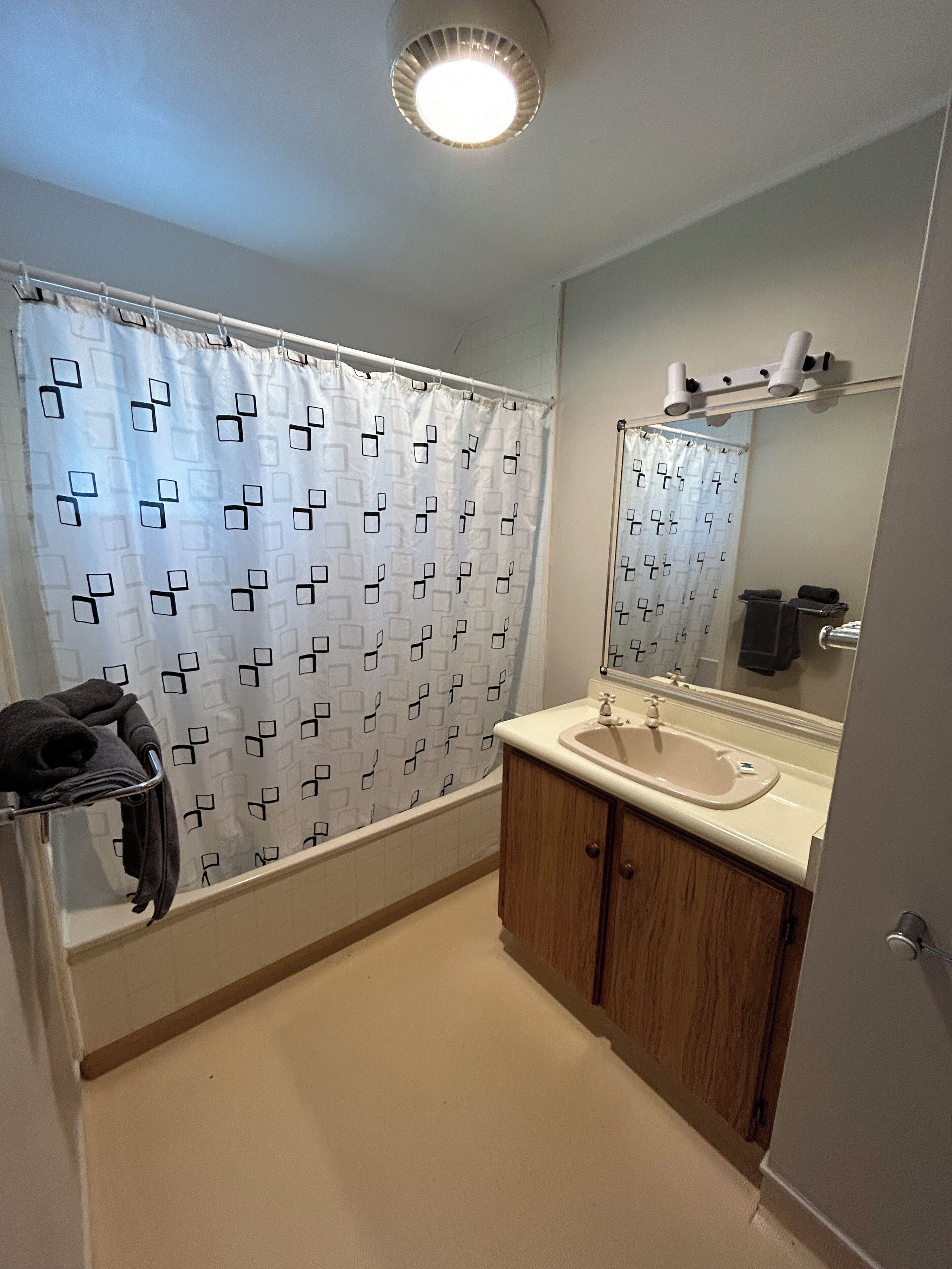 A bathroom with a shower curtain, a sink, a mirror, and a towel rack.