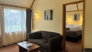 A room with a sofa, a coffee table, and a bed. There are wall-mounted lights and a window with curtains.
