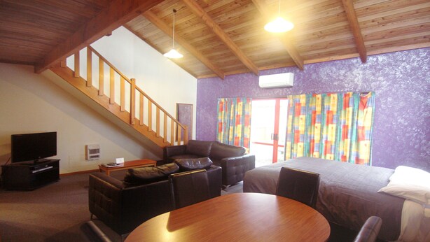 Una habitación con techo de madera, una escalera, una cama, un sofá, un televisor y una mesa.