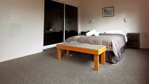 Un dormitorio con cama, una banca, una mesita de noche, un aparador y una puerta corrediza.