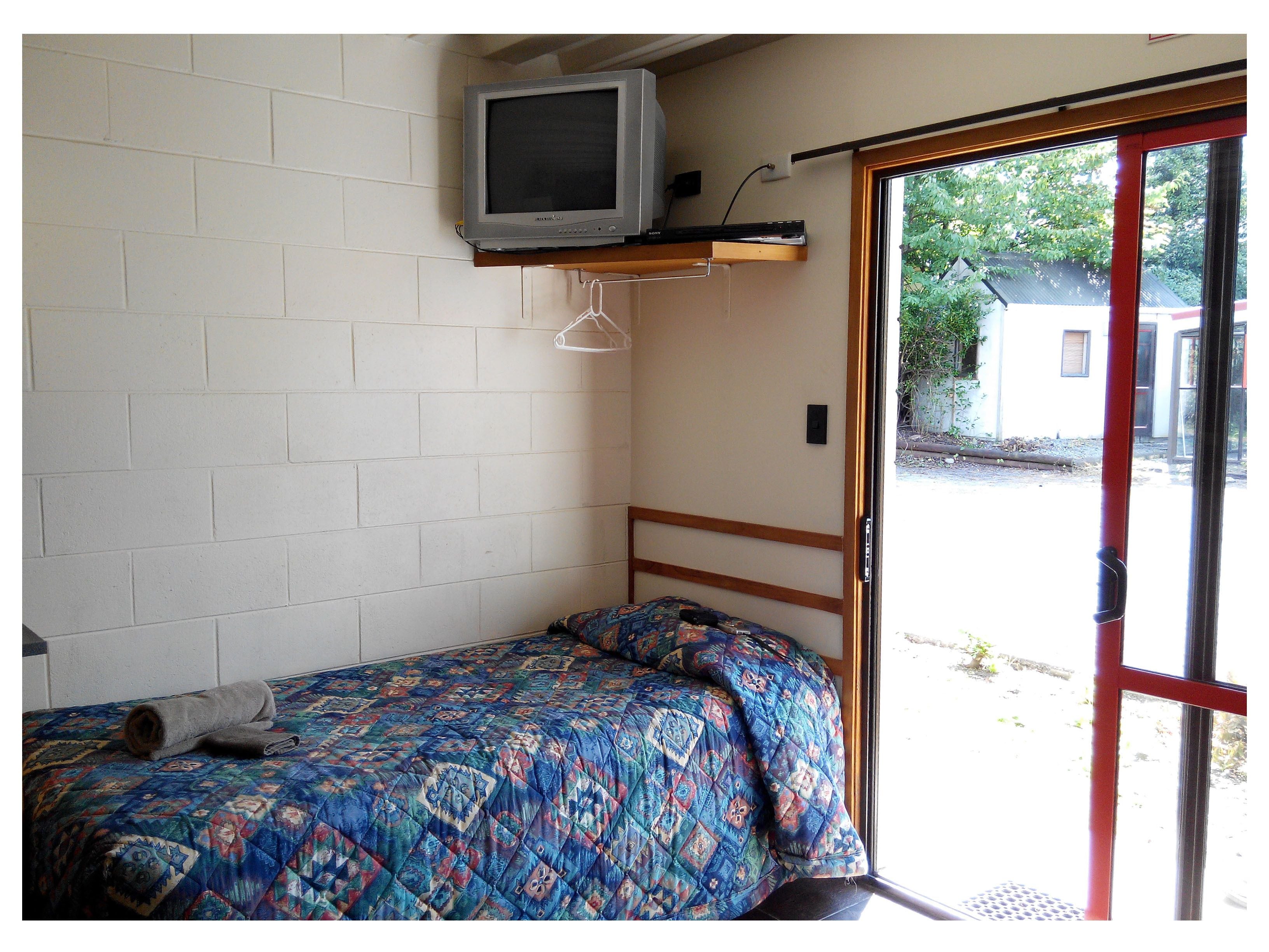 A small room with a bed, a television mounted on the wall, and a sliding glass door leading outside.