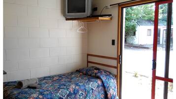 A small room with a bed, a television mounted on the wall, and a sliding glass door leading outside.