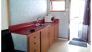 Una cocina compacta con encimera roja, un lavamanos, armarios de madera, microondas y una ventana sobre el lavamanos.