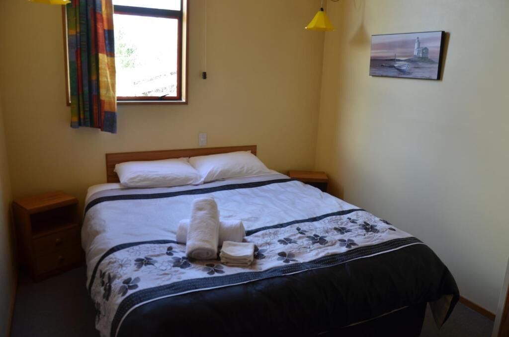 A neatly made bed with a floral bedspread, a set of towels, and a painting of a lighthouse on the wall.
