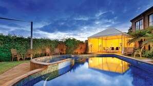 Una piscina con borde de azulejos, una zona de estar cubierta y un edificio con grandes ventanales.