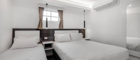 Quarto de hotel com duas camas de solteiro, um espelho grande, um ar condicionado e uma janela com cortinas.